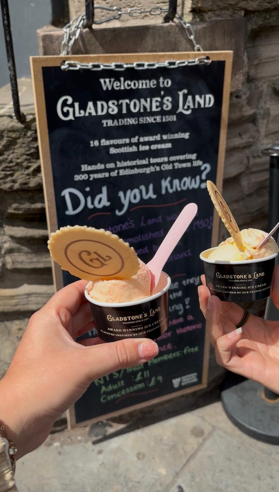 Two ice creams held in front of a sign